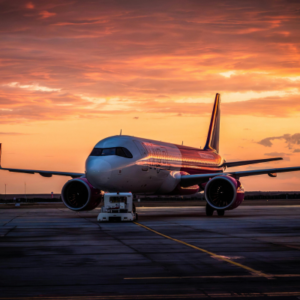 Commercial airliner parked on the tarmac at sunset, warm orange sky.