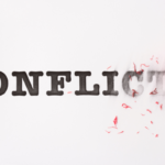 Hand holding a red heart erases the word 'CONFLICT,' symbolizing ending conflict or choosing peace.