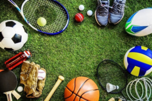 Assortment of sports gear on a grass field: soccer ball, basketball, volleyball, tennis racket, baseball bat and glove, shuttlecock, rugby ball, sneakers, and other equipment.