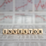 Wooden letter blocks spell INVESTOR on a newspaper with stock charts in the background.