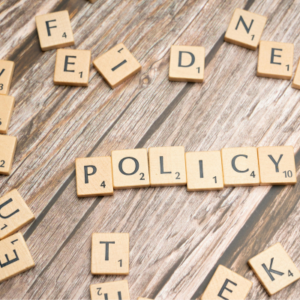 Scrabble tiles spell 'POLICY' on a wooden table, with scattered letters around.