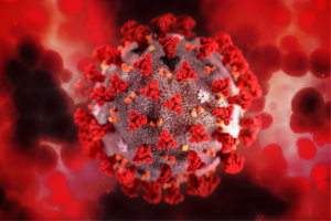 Close-up illustration of a coronavirus particle with red spike proteins against a red, blurred background.