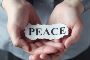 Two hands cupping a torn paper strip that reads PEACE, symbolizing peace.