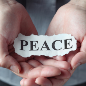 Two hands cupping a torn paper strip that reads PEACE, symbolizing peace.
