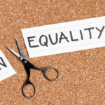 Scissors cut away the word 'IN' from a card that says 'EQUALITY', symbolizing removing inequality to achieve equality.