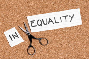 Scissors cut away the word 'IN' from a card that says 'EQUALITY', symbolizing removing inequality to achieve equality.
