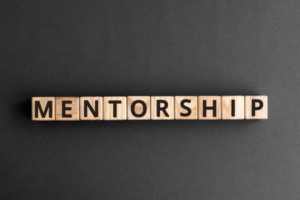 Wooden letter blocks spell 'MENTORSHIP' on a dark surface, illustrating the concept of mentorship.