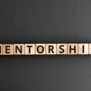 Wooden letter blocks spell 'MENTORSHIP' on a dark surface, illustrating the concept of mentorship.
