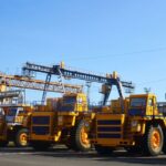 Row of bright yellow heavy-duty dump trucks parked on an industrial site under a clear blue sky.