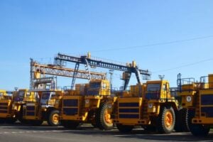 Row of bright yellow heavy-duty dump trucks parked on an industrial site under a clear blue sky.