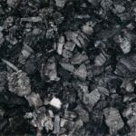 Close-up of irregular black coal chunks and charcoal fragments on a dark surface.