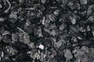 Close-up of irregular black coal chunks and charcoal fragments on a dark surface.
