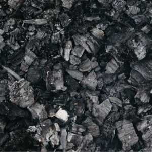 Close-up of irregular black coal chunks and charcoal fragments on a dark surface.