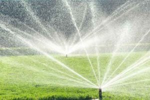 Ground sprinklers spraying water in multiple directions across a green lawn, creating arcs of spray.