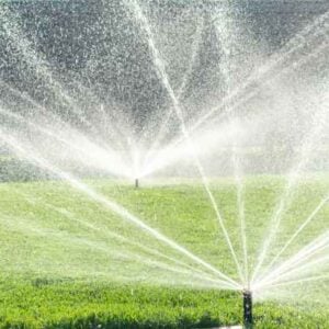 Ground sprinklers spraying water in multiple directions across a green lawn, creating arcs of spray.