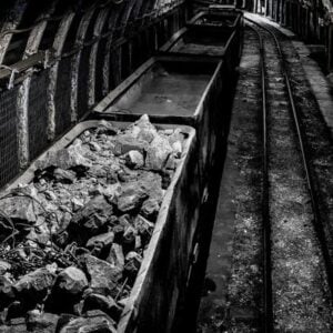 Underground mining tunnel with a ore cart filled with rocks on narrow rails.