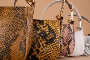 Row of snakeskin-pattern handbags in yellow, brown, pink, and gray hues on display.