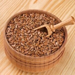 Flax seeds in a wooden bowl with a small wooden scoop on a light wooden surface, ready for scooping.