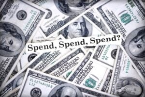 Pile of US $100 bills with a banner reading 'Spend, Spend, Spend?'.