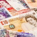 Pile of assorted British pound banknotes (£10, £20, £50) overlapping in a colorful collage.