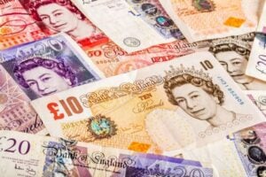 Pile of assorted British pound banknotes (£10, £20, £50) overlapping in a colorful collage.