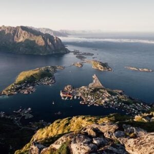 Coastal village tucked in a fjord, with boats and colorful houses, surrounded by rugged mountains and blue water (overhead view).