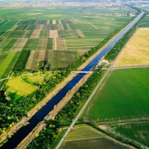 Aerial view of a canal cutting through patchwork farmland with roads and fields in varying greens and yellows to either side.