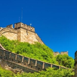 Section of the Great Wall winding over green hills under a clear blue sky, ancient stone battlements visible